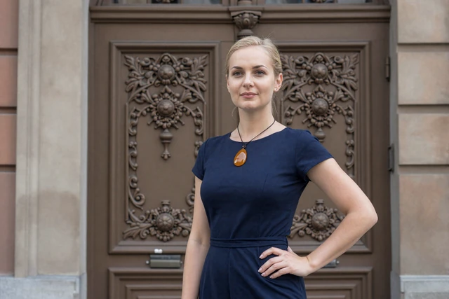 Elegant Latvian woman wearing an amber necklace standing in front of an ornate Art Nouveau doorway in Riga