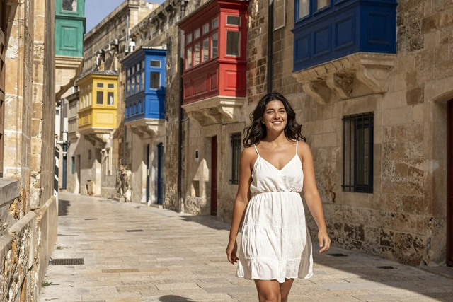 Attractive Maltese woman walking through a historic Valletta street with traditional colorful wooden balconies