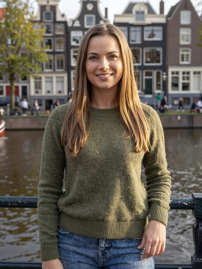 Katrien, 29, Dutch woman smiling warmly by an Amsterdam canal with historic houses behind