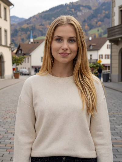 Anna, 27, a blonde Liechtenstein woman smiling on a cobblestone street in Vaduz with Alpine mountains behind her